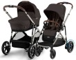 Wózek Cybex Gazelle S w konfiguracji dla bliźniąt lub rodzeństwa, z dwiema gondolami. Wózek jest w kolorze Chocolate Brown, z beżowym stelażem i brązowymi skórzanymi rączkami.