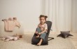 Starsze dziecko siedzi w szarym leżaczku BabyBjörn, który jest ustawiony w pozycji pionowej i pełni funkcję fotelika. Dziecko ma związane włosy, uśmiecha się i patrzy przed siebie.