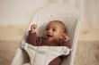 Bardzo bliskie ujęcie uśmiechniętego niemowlęcia w leżaczku BabyBjörn. Niemowlę ma szeroko otwarte, zadowolone usta i podniesione rączki.