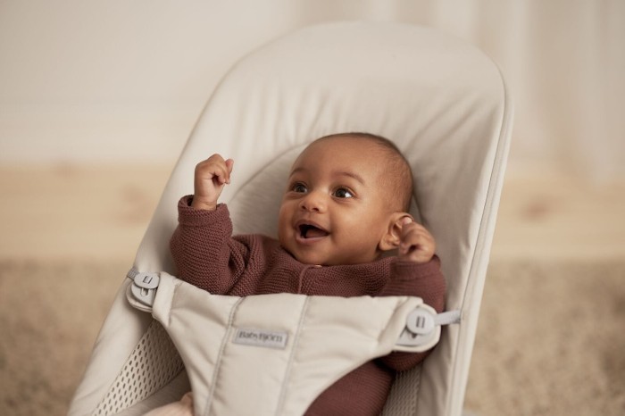 Bardzo bliskie ujęcie uśmiechniętego niemowlęcia w leżaczku BabyBjörn. Niemowlę ma szeroko otwarte, zadowolone usta i podniesione rączki.
