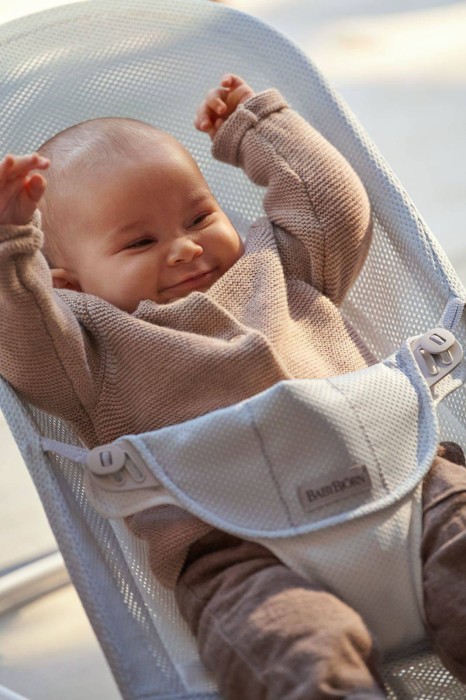 Bardzo bliskie ujęcie roześmianego niemowlęcia w leżaczku BABYBJÖRN MESH, z rączkami uniesionymi w geście radości. Widać siateczkową strukturę materiału.