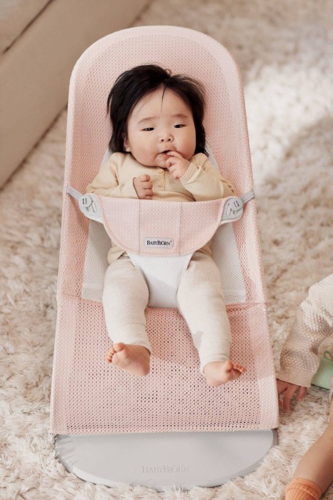 Niemowlę w leżaczku BABYBJÖRN (różowy Mesh) ustawionym w najwyższej pozycji. Dziecko leży na wznak. Widoczny detal pasów bezpieczeństwa i logo BABYBJÖRN.