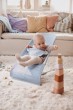 Niemowlę w leżaczku BABYBJÖRN (błękitny Mesh) w jasnym salonie. Leżaczek ustawiony jest w średniej pozycji, obok stoi wieża z klocków.