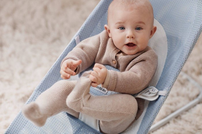 Zbliżenie niemowlęcia w leżaczku BABYBJÖRN (błękitny Mesh), bawiącego się własnymi nóżkami. Dziecko w dzianinowym ubranku. Kadr podkreśla swobodę ruchów.