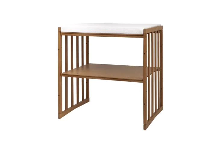 Łóżeczko Waldin 7w1 Owal-V Vintage w konfiguracji przewijaka z półką na dole i materacykiem na blacie. Drewniana konstrukcja w ciepłym kolorze vintage pasuje do pokoju niemowlęcia.